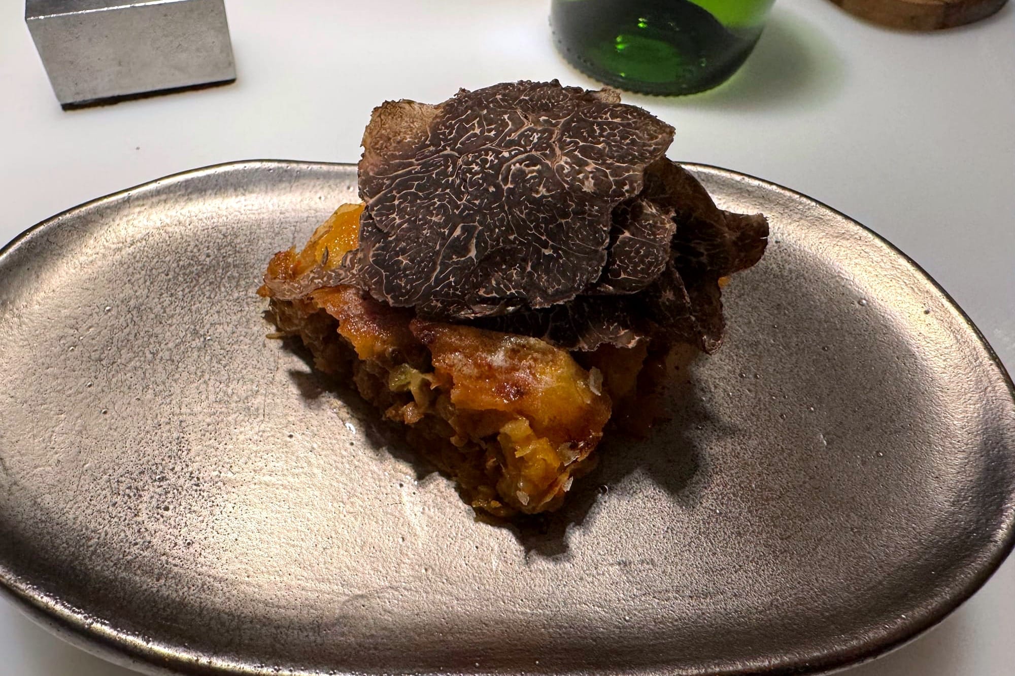 Close-up of a golden, flaky börek filled with kimchi, finished with thin shavings of black truffle.