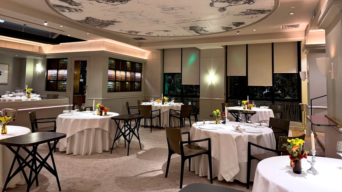 Elegant dining room at Restaurant Pierre Gagnaire in Paris, with round tables, white tablecloths and the signature illustrated ceiling.