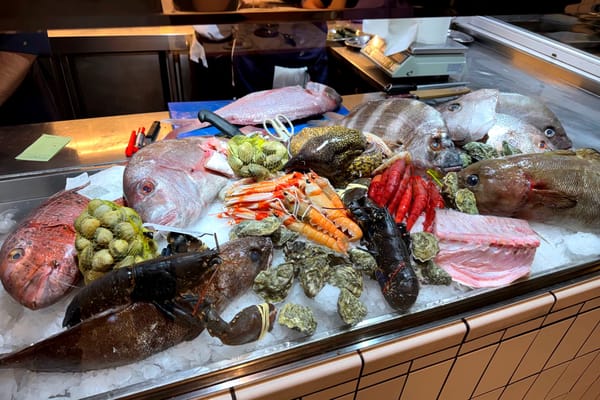 Display of whole fish, lobsters, prawns, clams, and oysters on crushed ice behind glass at the restaurant entrance.